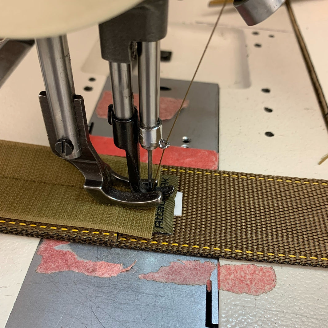 Sewing machine needle stitching a brown fabric strip on a flat surface.